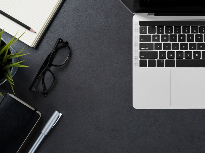 Crni radi sto sa naočarima, laptopom, beležnicom, olovkom. 